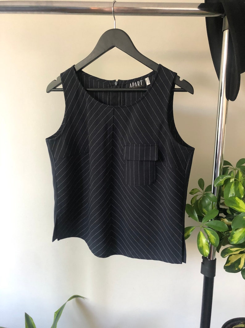 Puede incluir: Una blusa sin mangas de rayas blancas y negras con un bolsillo en la parte delantera. La blusa tiene la palabra "APART" impresa en la etiqueta.