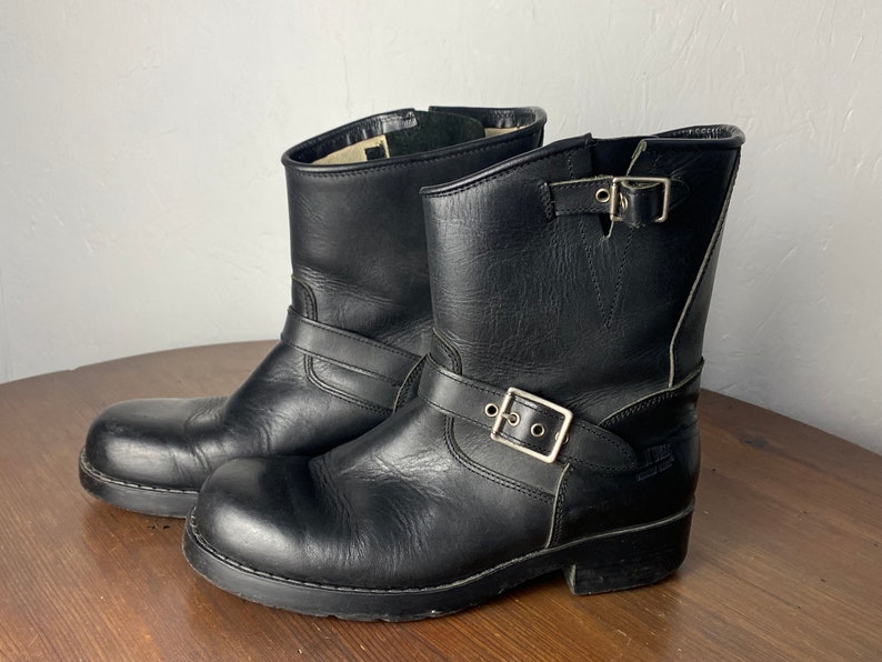 May include: A pair of black leather ankle boots with buckles. The boots have a chunky heel and a rounded toe.