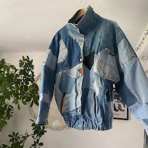 Puede incluir: Chaqueta vaquera patchwork en varios tonos de azul. La chaqueta presenta un cuello alto, cierres de botón y múltiples bolsillos. Tiene un parche de cuero marrón y un parche negro. La chaqueta mide aproximadamente 71 cm de largo.