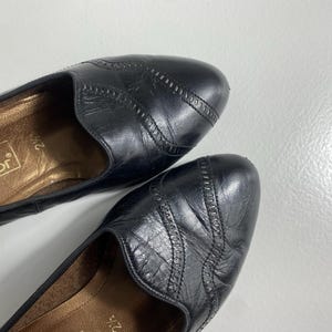 May include: A pair of black leather flats with decorative stitching on the toe. The shoes have a low heel and a gold-toned insole. The brand name "Gabor" is visible inside one shoe. The shoes are size 7 1/2.