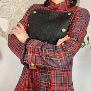 Puede incluir: Una camisa de cuadros rojos y negros con cuello de piel sintética negra y botones dorados. La camisa tiene un gran parche negro en la parte delantera con botones dorados.