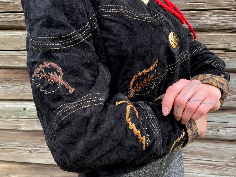 May include: A black suede jacket with gold stitching and brown embroidered leaves. The jacket has a button closure and a stand-up collar.