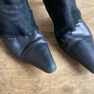 Può includere: Un paio di stivaletti neri in pelle scamosciata e pelle con punta a punta e un dettaglio cucito intorno alla caviglia.