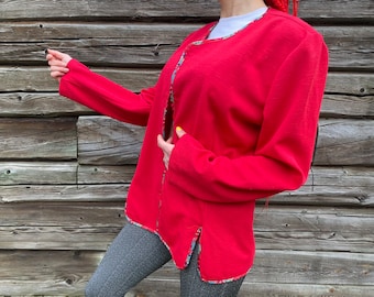 Puede incluir: Una chaqueta roja de manga larga con ribete floral. La chaqueta tiene un cuello chal y un corte holgado.