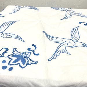 Puede incluir: Mantel blanco con pájaros y diseños florales bordados en azul.