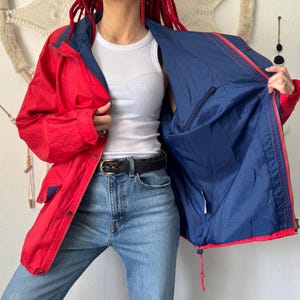 Puede incluir: Chaqueta reversible roja y azul marino con cremallera. El exterior es rojo con detalles azul marino, y el interior es azul marino. Fabricada con un material ligero, presenta un diseño clásico.