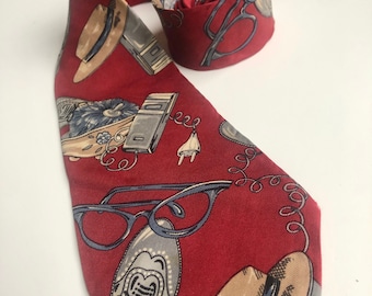 May include: A red silk tie with a pattern of eyeglasses, shoes, telephones, and hats. The tie is in a folded position.
