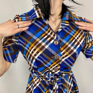 May include: A blue, brown, and white plaid dress with a collared neckline, short sleeves, and a button-up front. The dress has a belt at the waist.