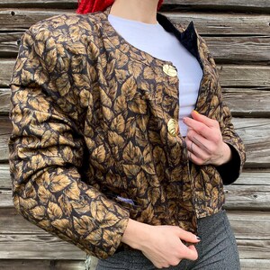 May include: A brown and gold leaf patterned jacket with gold buttons. The jacket has a cropped length and long sleeves.