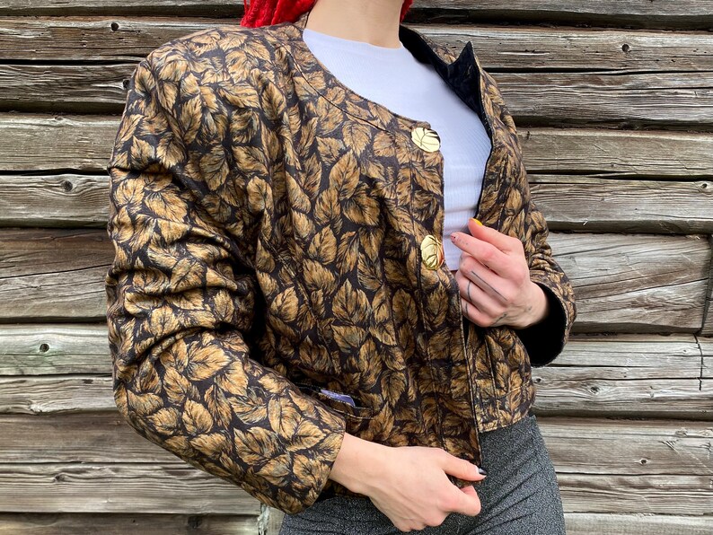 May include: A brown and gold leaf patterned jacket with gold buttons. The jacket has a cropped length and long sleeves.