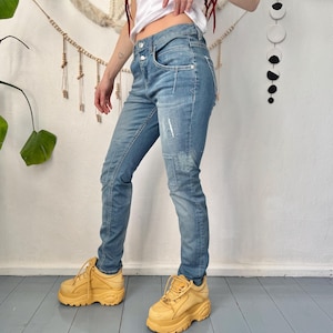May include: Light blue denim jeans with distressed patches and a classic five-pocket design. The jeans are paired with chunky, platform-soled, yellow sneakers. The overall look is casual and stylish.