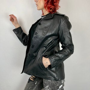 May include: Black leather jacket with a collar and button closure. The jacket has a fitted silhouette and a slightly cropped length.