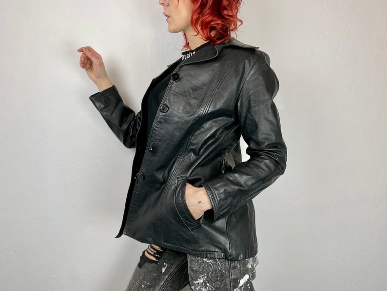 May include: Black leather jacket with a collar and button closure. The jacket has a fitted silhouette and a slightly cropped length.