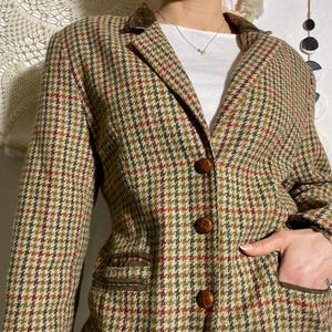 Peut inclure: Un blazer à carreaux marron, vert et rouge avec un col cranté et trois boutons marron. Le blazer a deux poches avant avec une garniture marron et un col en velours marron.