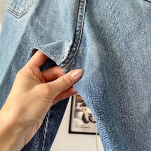 May include: Light blue denim jeans with a classic five-pocket design. The jeans show signs of wear and tear, with visible fading and distressing. The image highlights the texture and details of the denim fabric, showcasing the stitching and pocket design.