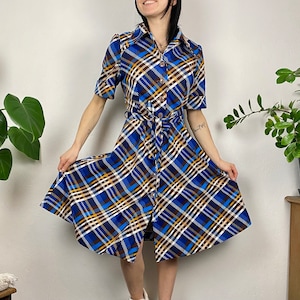 May include: A blue, white, and brown plaid dress with a button-up front and a belt. The dress has a short sleeve and a flared skirt.