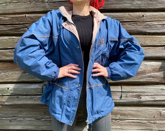 May include: A blue and beige jacket with brown stitching and a zipper closure. The jacket has a hood and a drawstring waist.