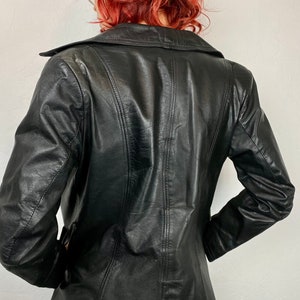 May include: A black leather jacket with a long, fitted style. The jacket has a collar and a button closure.