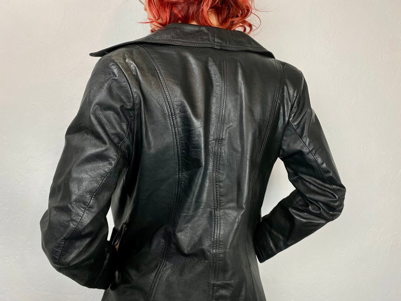 May include: A black leather jacket with a long, fitted style. The jacket has a collar and a button closure.