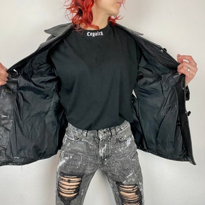 May include: A black leather jacket with a button closure and a black lining. The jacket is open and the lining is visible. The jacket has a collar and two pockets on the front.