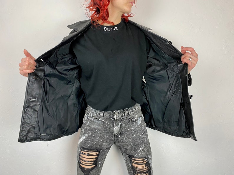 May include: A black leather jacket with a button closure and a black lining. The jacket is open and the lining is visible. The jacket has a collar and two pockets on the front.
