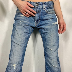 May include: Distressed blue denim jeans with several small rips and tears throughout the fabric.