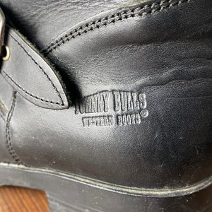 May include: Close-up of a black leather boot with a buckle strap and the text "JOHNNY BULLS WESTERN BOOTS" embossed on the side.
