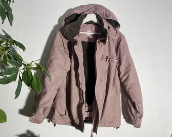 May include: A mauve and white striped hooded jacket with a black interior. The jacket has a zip closure, two front pockets, and a drawstring hood. The jacket is hanging on a white wall.