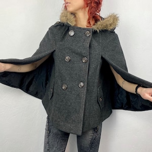 May include: A gray cape coat with a faux fur-lined hood and double-breasted button closure. The coat has a cape design with arm openings and two front pockets. The lining is black.