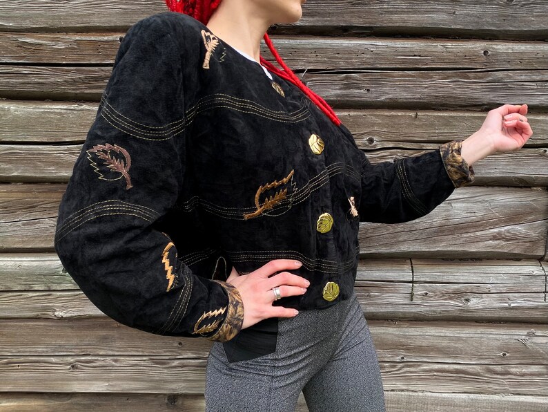 May include: A black suede jacket with gold buttons and leaf embroidery. The jacket has a cropped fit and a relaxed silhouette.