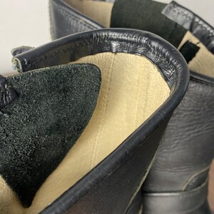 May include: Close-up of the inside of a black leather boot. The boot has a beige lining and a black suede insole.