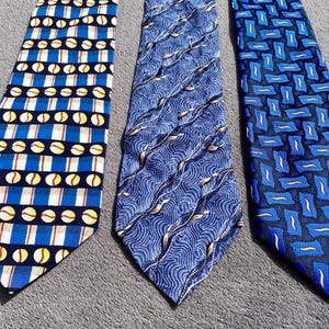 Può includere: Tre cravatte fantasia. La prima presenta un motivo a righe blu e bianche con cerchi gialli. La seconda ha un motivo a onde blu. La terza ha un design geometrico blu.