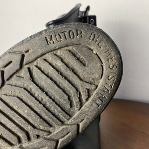 May include: Close-up of the black rubber sole of a boot with a tread pattern and the text "MOTOR OIL RESISTANT" embossed on the sole.