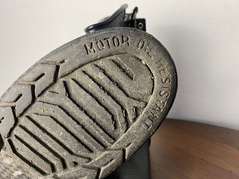 May include: Close-up of the black rubber sole of a boot with a tread pattern and the text "MOTOR OIL RESISTANT" embossed on the sole.