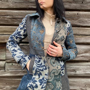Op de afbeelding: Een blauw en beige patchworkjas met een bloemenpatroon. De jas heeft lange mouwen en een kraag.