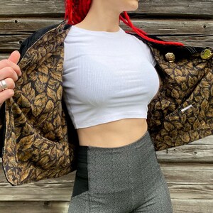 May include: A black jacket with a gold leaf patterned lining. The jacket is open and the lining is visible. The jacket has gold buttons.