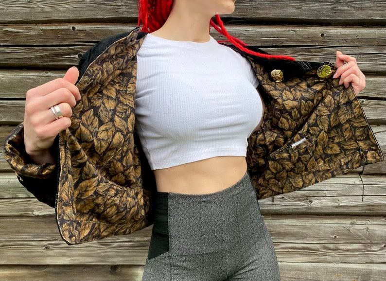May include: A black jacket with a gold leaf patterned lining. The jacket is open and the lining is visible. The jacket has gold buttons.