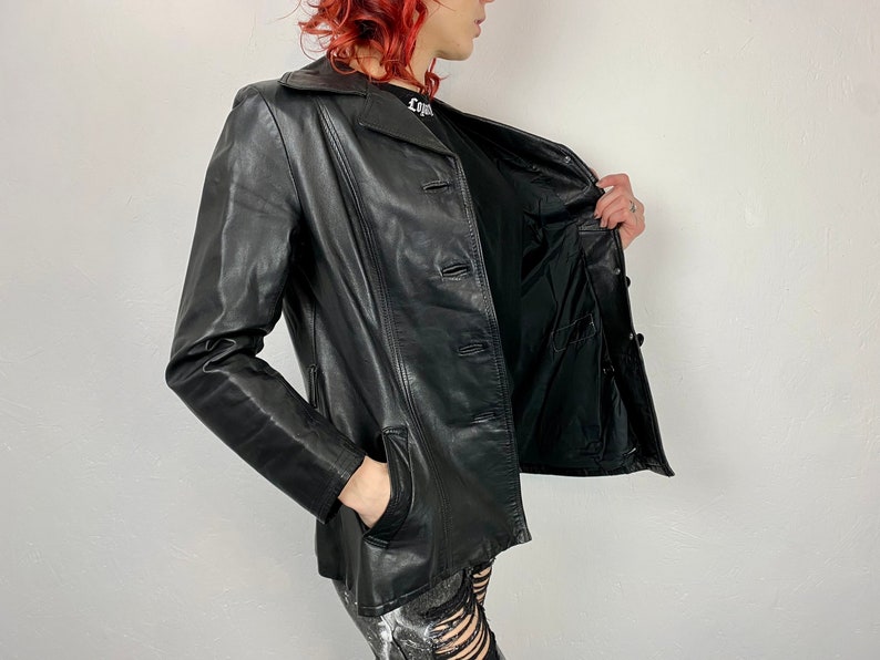 May include: A black leather jacket with a button closure and two pockets. The jacket is unzipped and the lining is visible.