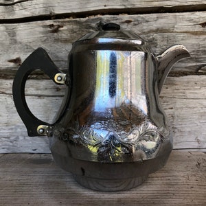 Pode incluir: Uma chaleira de prata com uma pega de plástico preto e um design floral. A chaleira está sobre uma superfície de madeira.