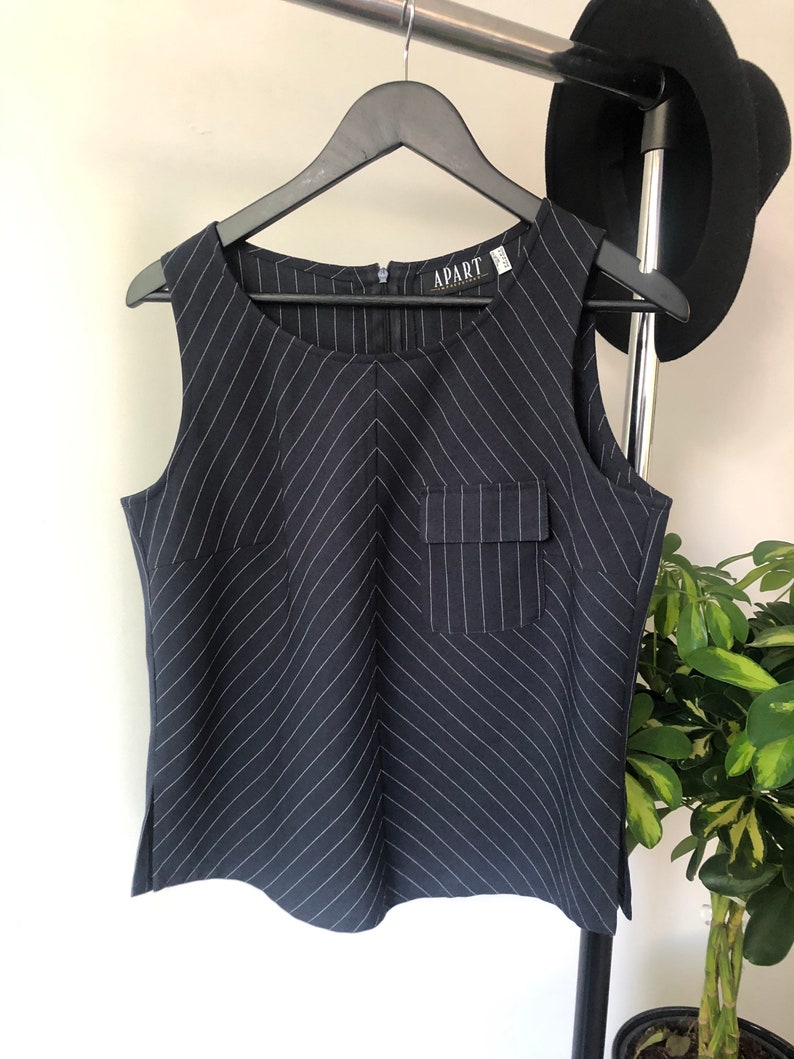 Puede incluir: Una blusa sin mangas de rayas blancas y negras con un bolsillo en la parte delantera. La blusa tiene una cremallera y la etiqueta "APART" es visible.
