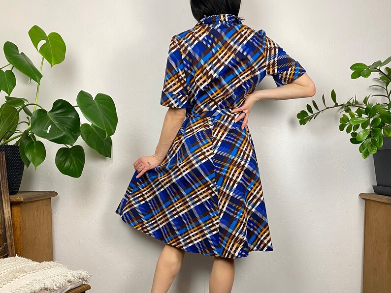 May include: A blue, brown, and white plaid dress with a short sleeve and a fitted bodice. The dress has a flared skirt and a belt.