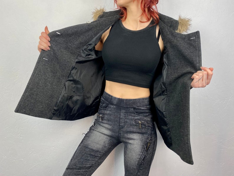 May include: A charcoal gray wool coat with a faux fur collar. The coat has a black satin lining and three white buttons. The model is wearing a black crop top and gray denim-look leggings.