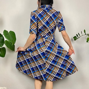 May include: A blue, white, brown, and yellow plaid dress with a short sleeve and a fitted bodice. The dress has a flared skirt and a belt.