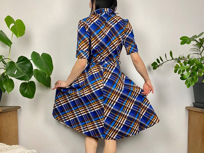 May include: A blue, white, brown, and yellow plaid dress with a short sleeve and a fitted bodice. The dress has a flared skirt and a belt.