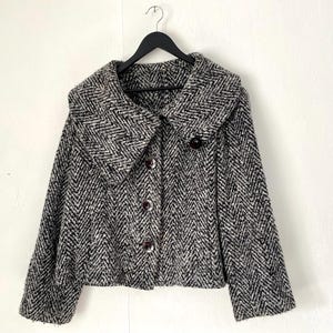 May include: A black and white herringbone patterned jacket with a large, wide collar and button closure.