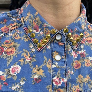 Könnte beinhalten: Ein blaues Jeanshemd mit Blumenmuster und einem goldenen, mit Nieten besetzten Kragen.