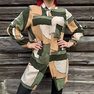 Könnte beinhalten: Ein langärmeliges Hemd mit Knopfleiste und einem geometrischen Muster in Olivgrün, Beige und Cremeweiß. Das Hemd verfügt über einen klassischen Kragen, eine durchgehende Knopfleiste vorne und einen geraden Saum, der über die Taille reicht.