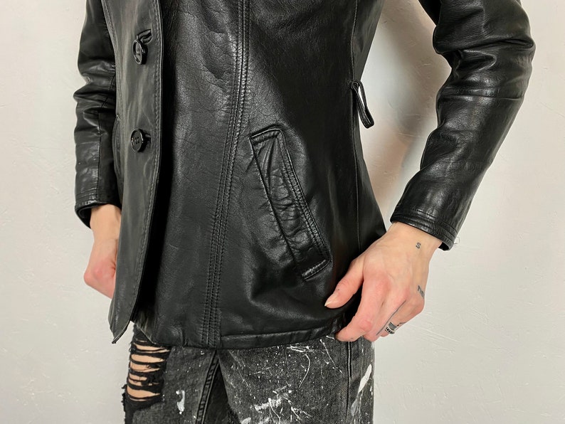 May include: A black leather jacket with a double-breasted closure and two buttons. The jacket has a pocket on the left side and a fitted silhouette.