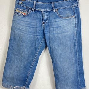 May include: A pair of blue denim cuffed shorts with a frayed hem. The shorts have a belt loop and a Diesel logo on the back pocket.