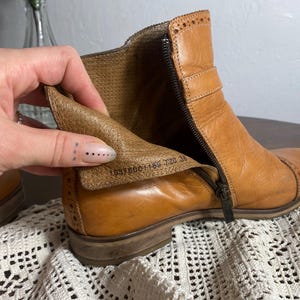 K&ouml;nnte beinhalten: Hellbraune Leder-Ankle Boots mit seitlichem Rei&szlig;verschluss und Ziern&auml;hten. Die Stiefel haben einen niedrigen Absatz und eine Schnalle. Das Innenfutter ist sichtbar. Gr&ouml;&szlig;e 36.
